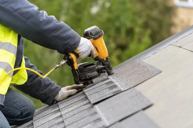 Technician replacing damaged shingles on a partially repaired roof