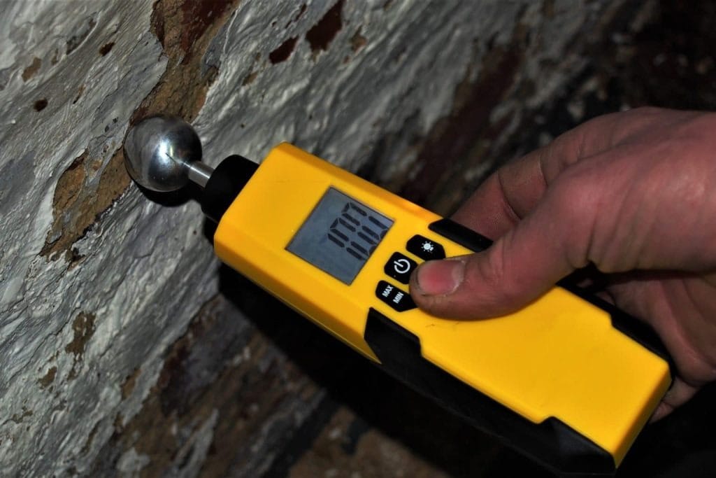 Technician using a moisture meter on baseboards during water damage restoration in a McKinney home