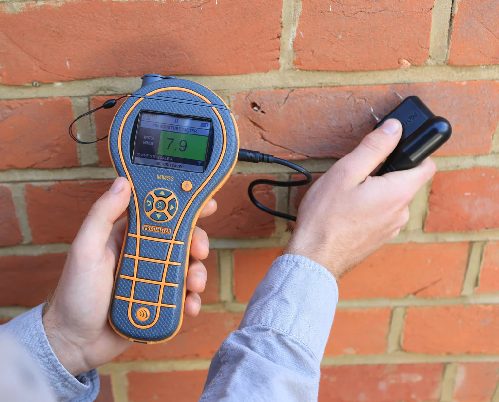 Technician using a moisture meter along the base of a wall to detect hidden water.
