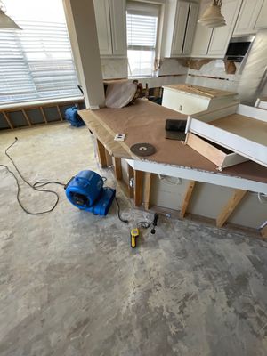 Kitchen with exposed lower cabinet framing, removed wall materials, air movers, cords, and tools on the floor.