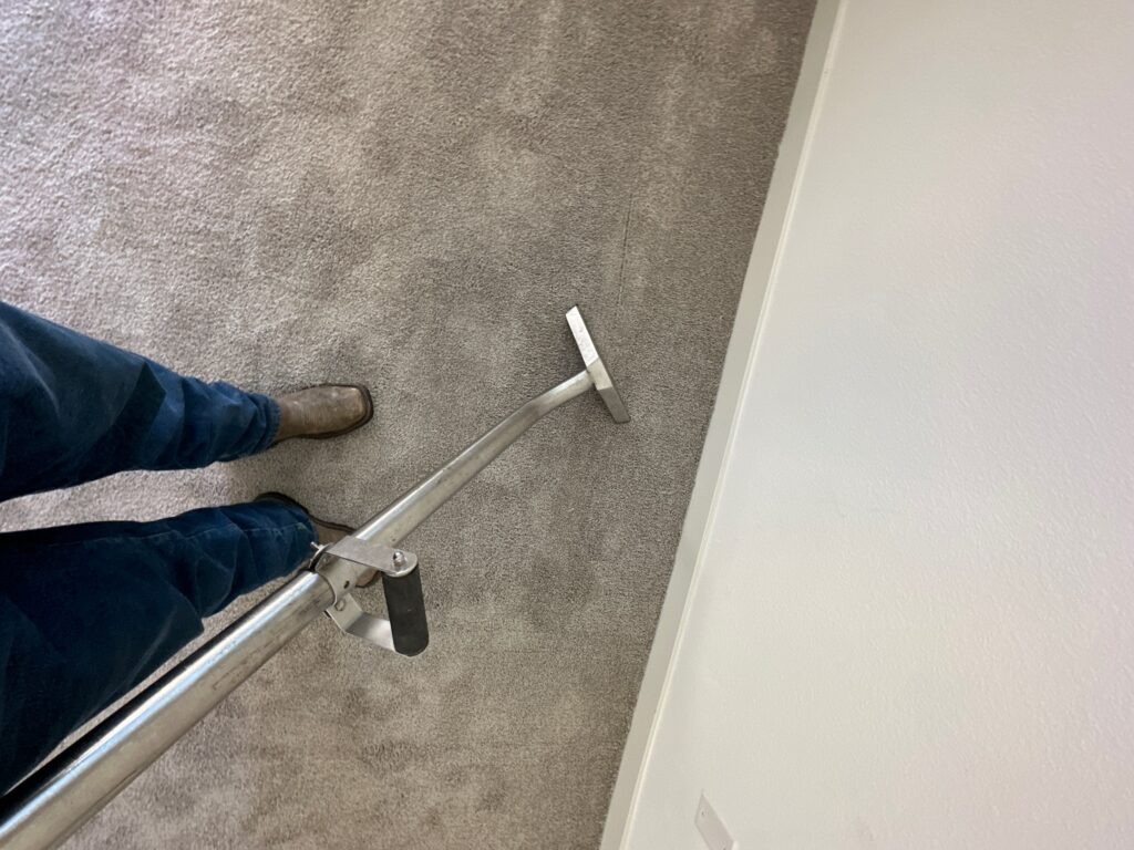 Technician operating a carpet extraction wand on damp flooring during water mitigation in Waxahachie, TX