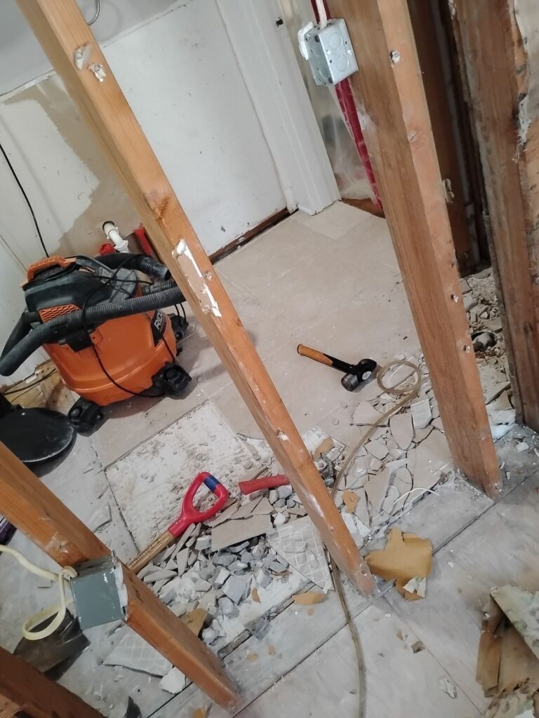 Bathroom demolition in Dallas, TX with exposed wall framing, broken tile, and remediation vacuum equipment