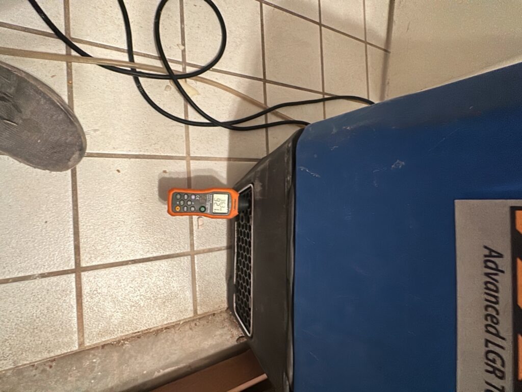 Moisture meter on a bathroom tile floor beside drying equipment during water mitigation in Plano, TX