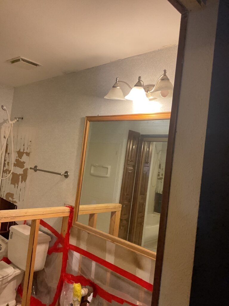 Bathroom in Plano, TX showing partial wall demolition and taped containment during water mitigation