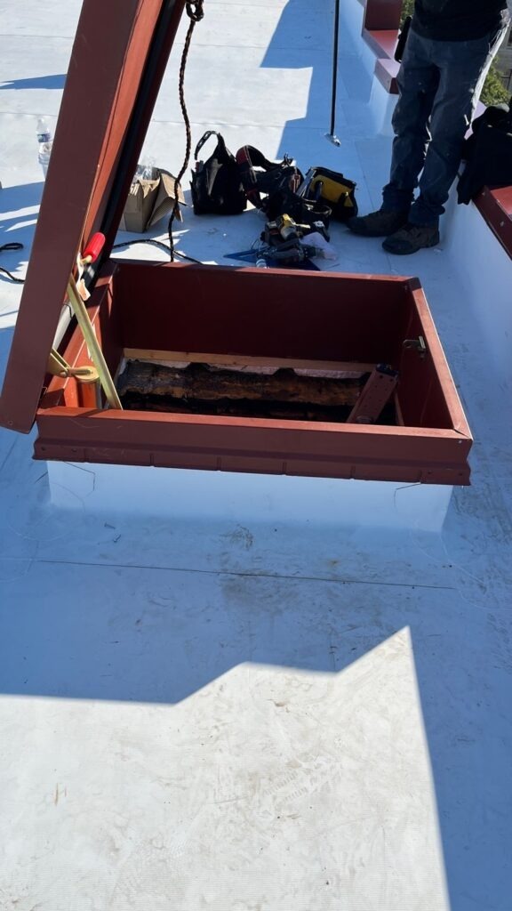 Open roof hatch set into a white TPO membrane commercial roof during roofing work in Bonham