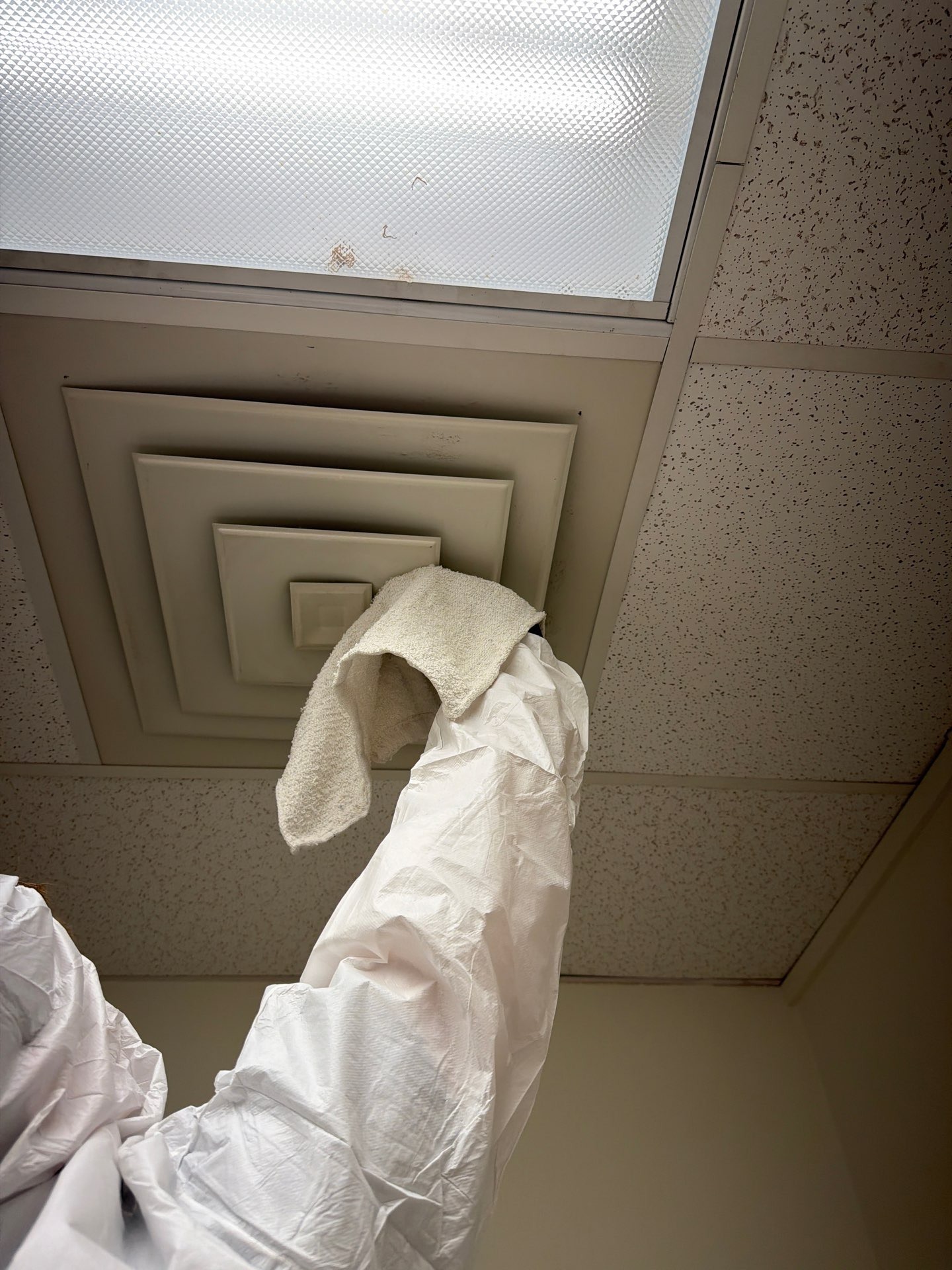 Protective-suited technician cleaning a ceiling HVAC vent during commercial mold remediation in Commerce, TX