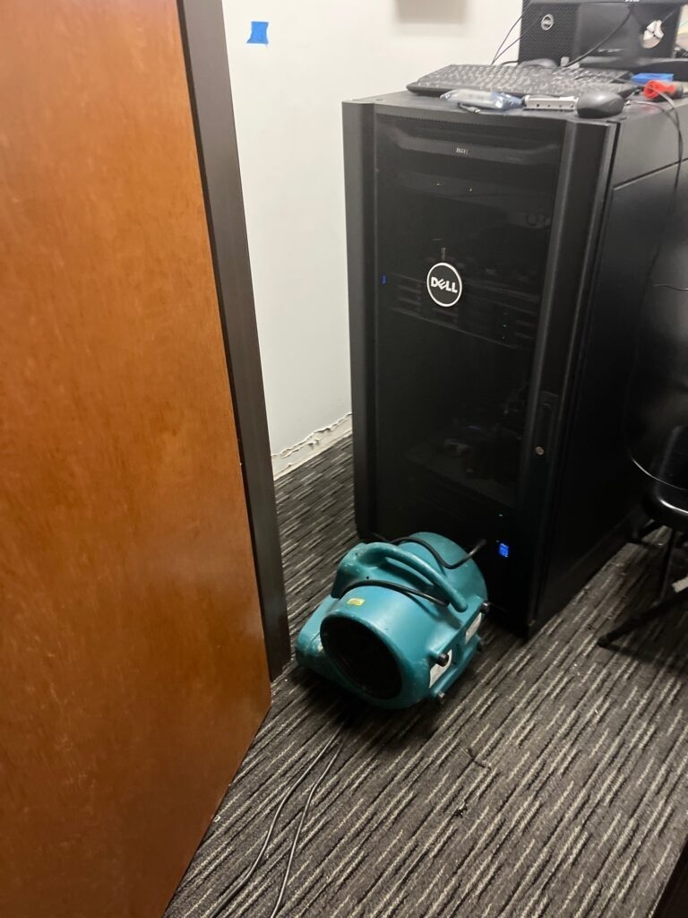 Air mover on office carpet beside equipment during water mitigation drying in Bonham, TX
