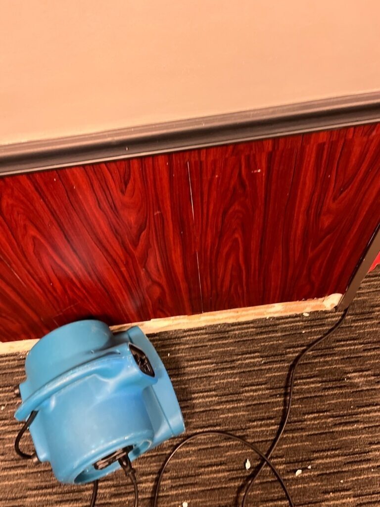 Blue air mover at the base of a wood-paneled wall for water mitigation drying in Bonham, TX