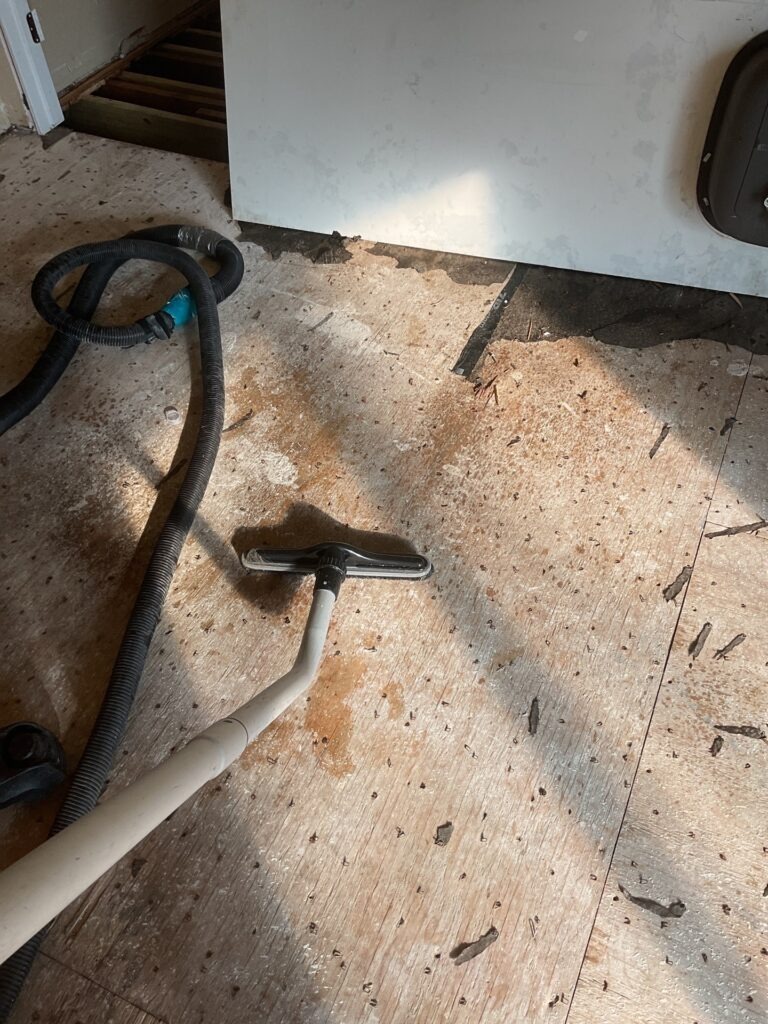 Subfloor demolition area in a Plano home with debris, exposed flooring surface, and extraction hose during mold remediation