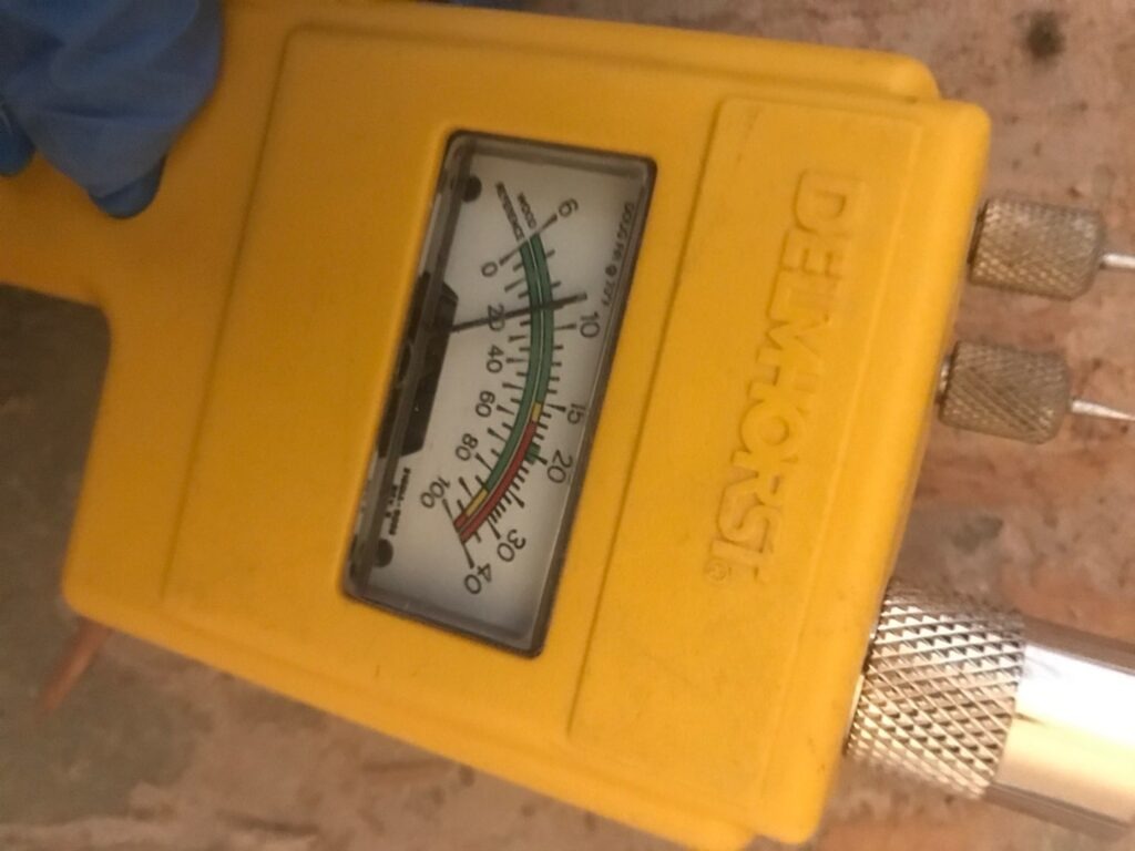 Handheld moisture meter pressed against an interior wall during water mitigation in McKinney, TX