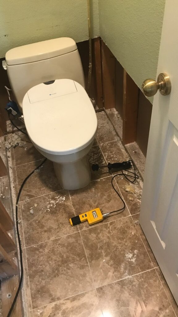 Bathroom floor and toilet area with removed baseboards and demolition debris during water mitigation in McKinney, TX