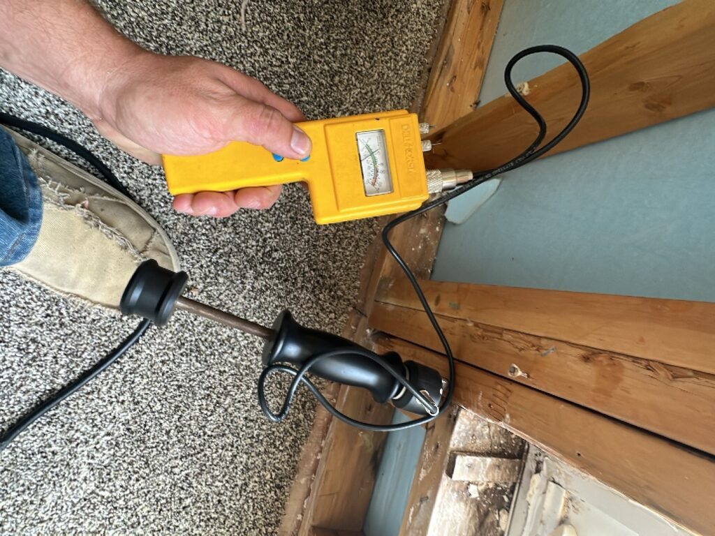 Technician using a moisture meter near exposed garage wall framing during water mitigation in McKinney, TX