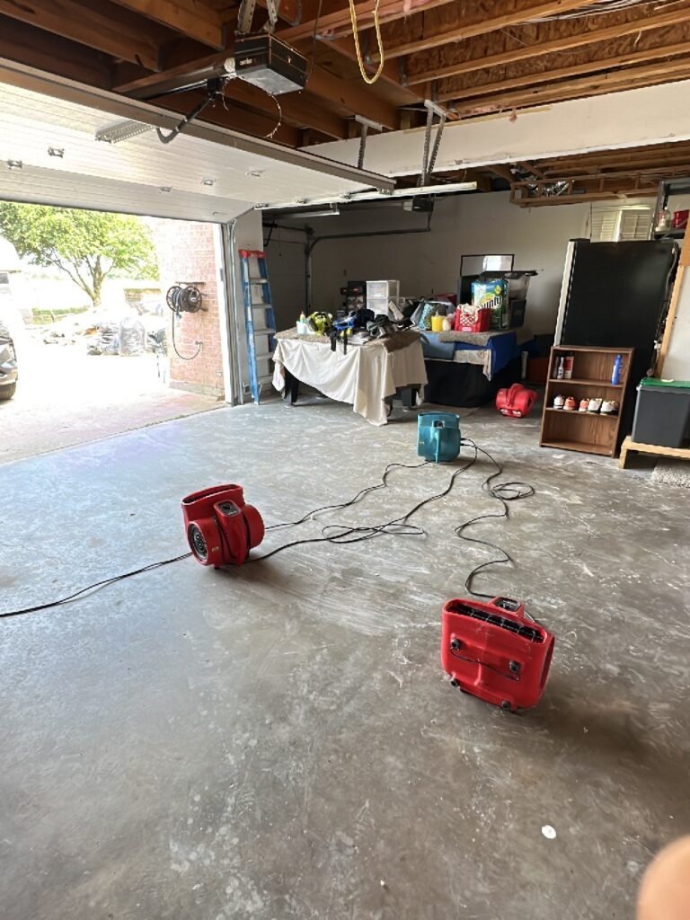 Air movers set up in a garage with exposed ceiling framing during water mitigation in McKinney, TX