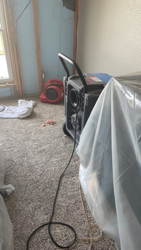Air mover and dehumidifier beside plastic-covered contents during garage water mitigation in McKinney, TX