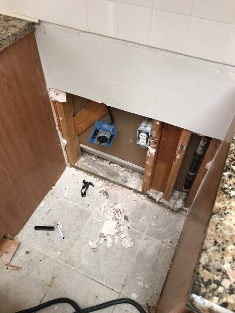 Kitchen cabinet base with lower panel removed to expose the wall cavity during water mitigation in Garland, TX