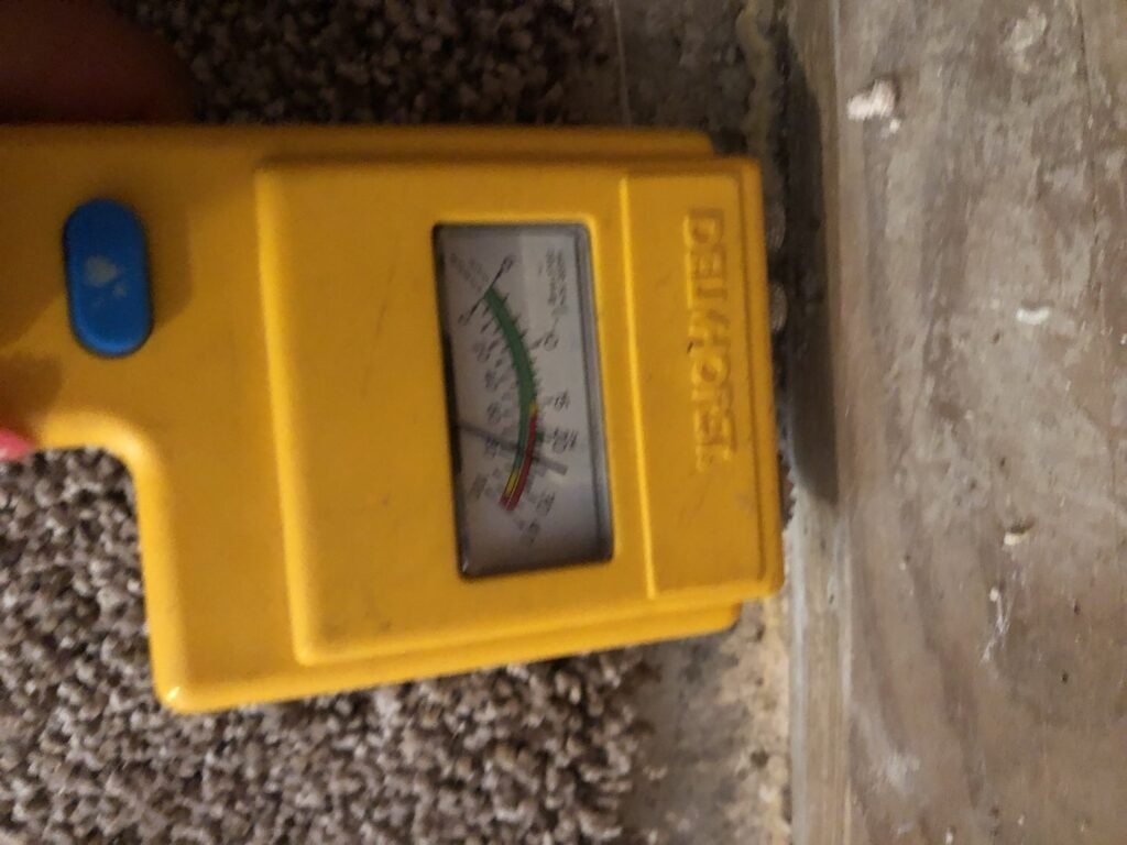 Moisture meter at the base of an interior wall during water mitigation in Garland, TX