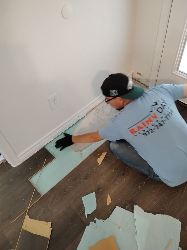 Technician removing damaged flooring along an interior wall during water mitigation in Princeton, TX