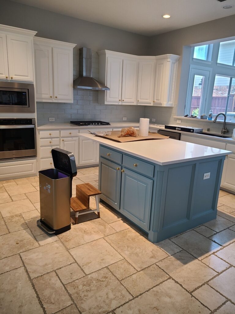 Residential kitchen in Allen, TX with white cabinets, blue island, and tile floor during restoration
