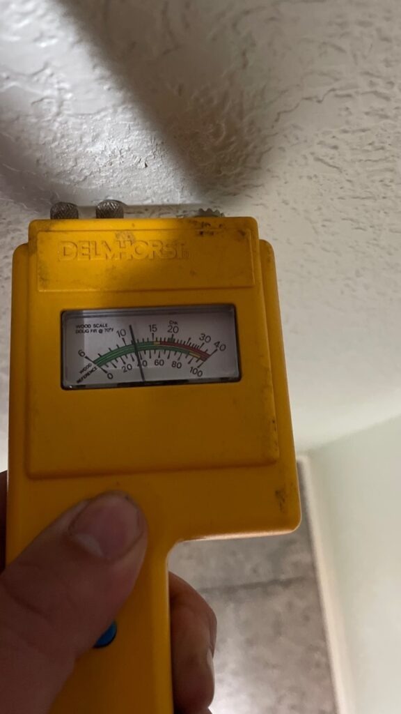Handheld moisture meter pressed against an interior ceiling during a water intrusion inspection in Van Alstyne, TX