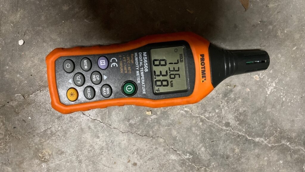 Handheld moisture meter displaying a reading on a concrete floor during water mitigation in McKinney, TX