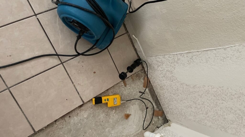 Air mover and moisture meter beside a water-damaged flooring edge in a McKinney, TX home