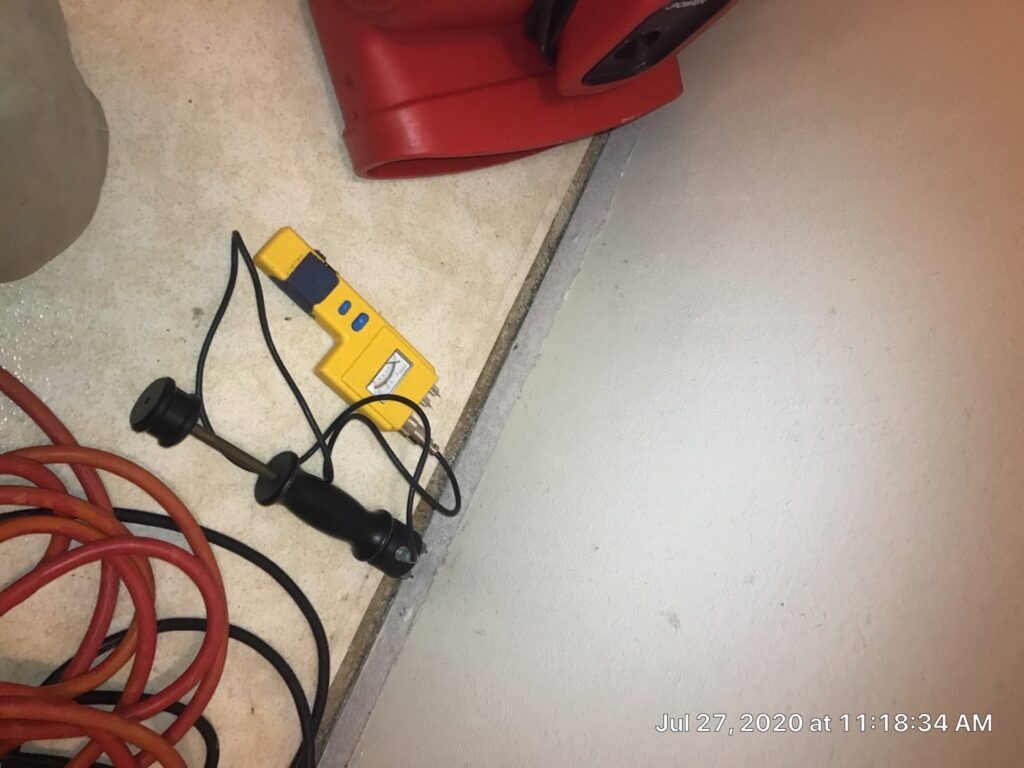Moisture meter and cords set beside an interior floor edge during water mitigation inspection