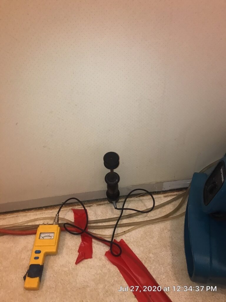 Moisture meter and probes set along a residential interior wall during water mitigation in Denison, TX