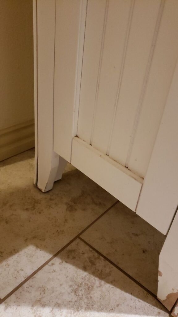Stained tile flooring and vanity base showing water damage in a Denton, TX bathroom