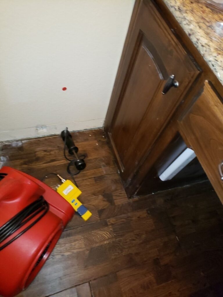 Air mover and moisture inspection tools beside damaged kitchen flooring and base cabinet in Denton, TX