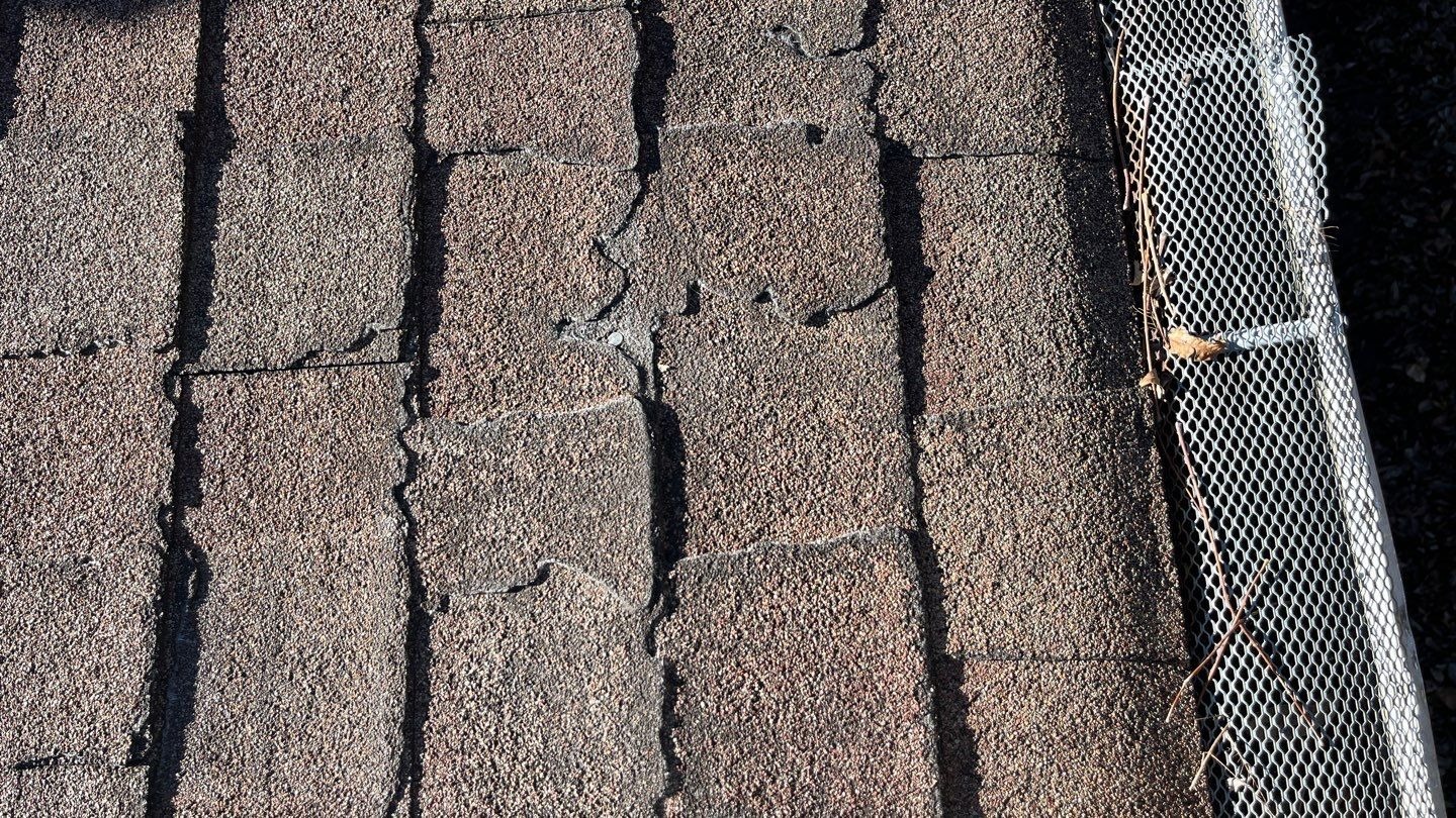 Hail impact marks visible on aging shingles before the roof repair in Sherman, TX